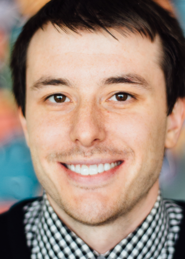 White male, dark brown hair, plaid blue shirt and dark sweater