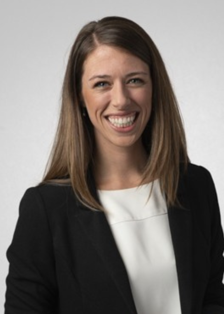 White woman, shoulder length brown hair, smiling, white shirt black jacket
