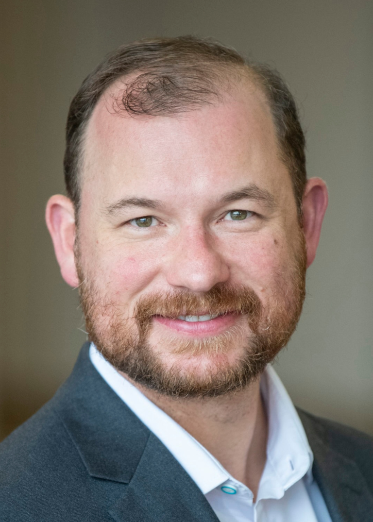 White man with baldness beginning, low cut beard, wearing suit jacket and collard shirt